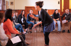 Photo of a choir leader clapping whilst teaching a group to sing