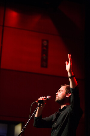 A photo of Zac Scott with a microphone and one hand in the air